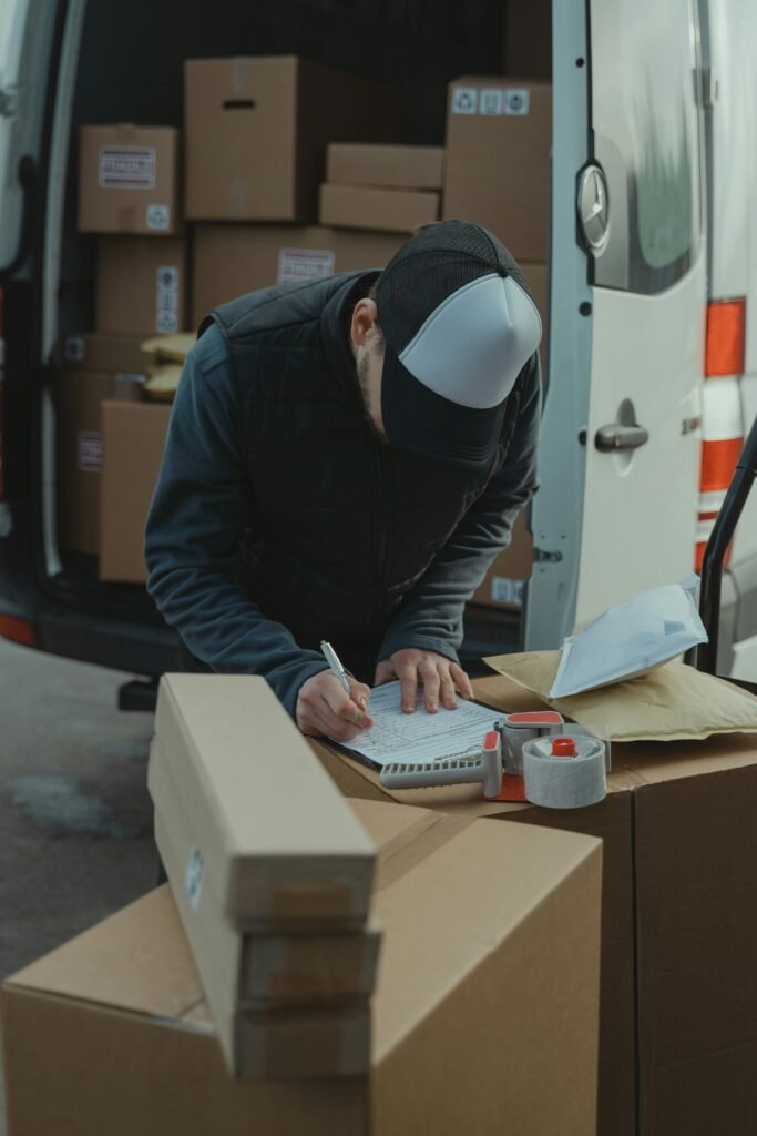 pexels photo 6169057 6169057 Courier organizing packages from a van, preparing for delivery in a logistics setting.